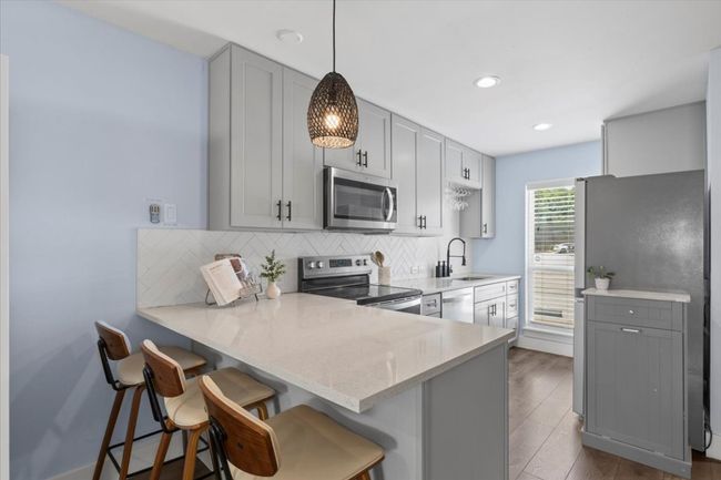 Kitchen featuring stainless steel appliances, gray cabinets, a kitchen breakfast bar, tasteful backsplash, and a peninsula | Image 7
