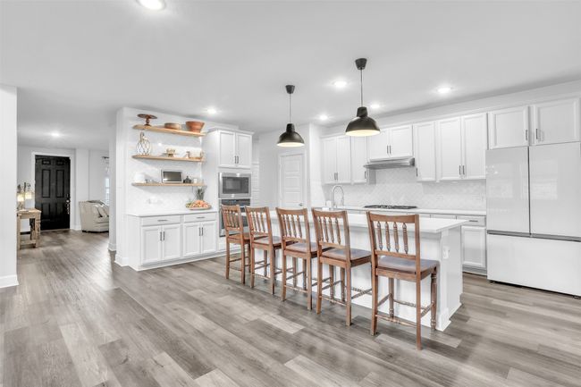 Kitchen featuring white cabinetry, decorative light fixtures, a kitchen island with sink, stainless steel appliances, and light hardwood / wood-style floors | Image 11