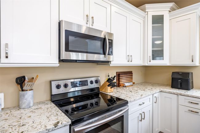 Kitchen with appliances with stainless steel finishes, light stone counters, white cabinetry, and glass insert cabinets | Image 12