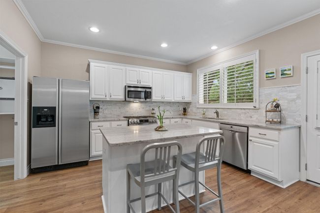 Kitchen with stainless steel appliances, a sink, white cabinetry, decorative backsplash, and crown molding | Image 9