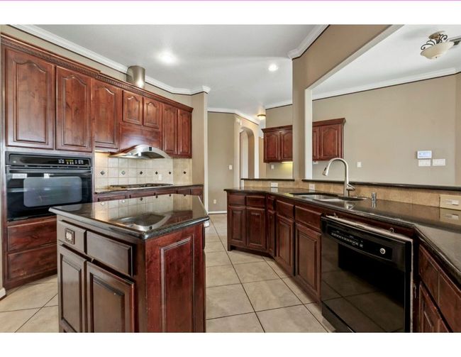 Kitchen featuring black appliances, tasteful backsplash, ornamental molding, light tile patterned floors, and a kitchen island | Image 19