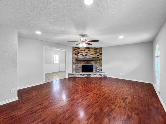 Unfurnished living room featuring ceiling fan, wood finished floors, a textured ceiling, a brick fireplace, and recessed lighting | Image 7