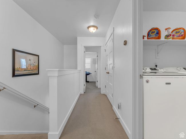 Hall with light colored carpet, washer and clothes dryer, and an upstairs landing | Image 24