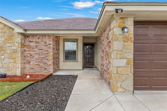 Doorway to property featuring roof with shingles, an attached garage, and brick siding | Image 5