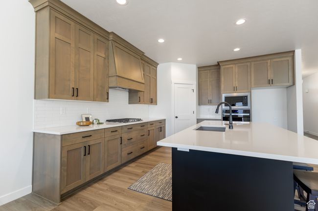 Kitchen with premium range hood, a sink, appliances with stainless steel finishes, decorative backsplash, and light wood-style floors | Image 5