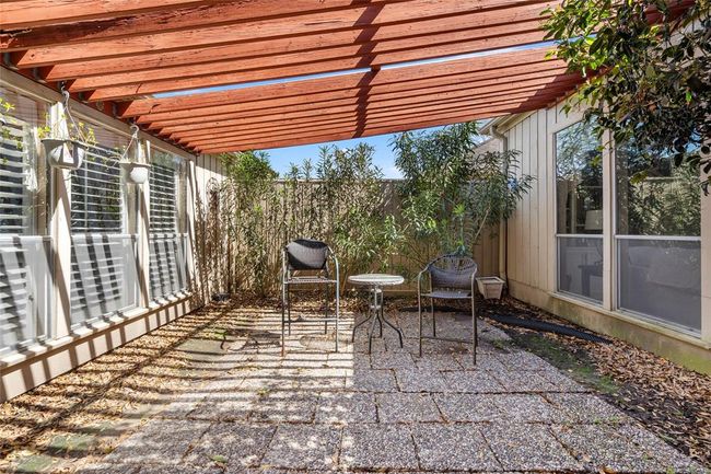This charming center courtyard offers a private outdoor retreat, complete with a pergola providing partial shade. Surrounded by lush greenery and enclosed for added privacy, the space is ideal for relaxing or enjoying a morning coffee. The pebble-stone patio enhances the natural ambiance, creating a cozy and inviting atmosphere. | Image 10