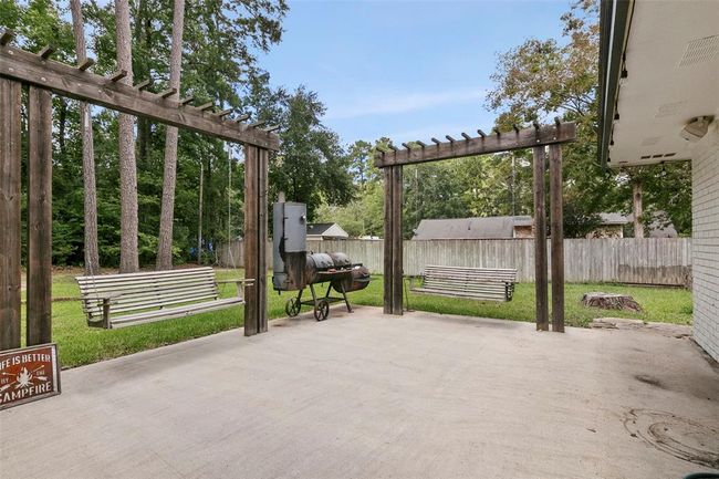 This backyard features a spacious concrete patio with wooden pergolas, two charming porch swings, and a barbecue grill, all surrounded by lush greenery and a wooden fence for privacy. Ideal for outdoor relaxation and entertaining. | Image 41