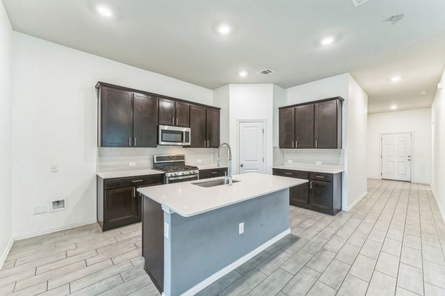 Kitchen featuring appliances with stainless steel finishes, wood finish floors, dark brown cabinets, tasteful backsplash, and recessed lighting | Image 4