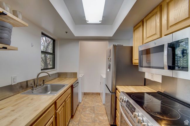 Kitchen featuring light brown cabinets, sink, a tray ceiling, appliances with stainless steel finishes, and butcher block counters | Image 9