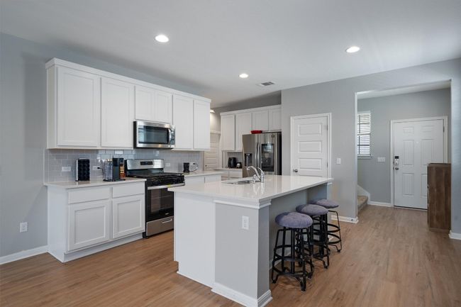 Kitchen featuring appliances with stainless steel finishes, tasteful backsplash, a kitchen bar, light wood-style flooring, and a kitchen island with sink | Image 4