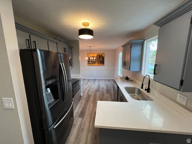 Kitchen with a sink, a chandelier, light countertops, black refrigerator with ice dispenser, and wood finished floors | Image 5
