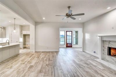 Unfurnished living room with light wood-type flooring, ceiling fan, a fireplace, and sink | Image 1