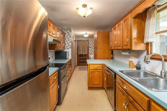 Kitchen featuring stainless steel appliances, under cabinet range hood, wallpapered walls, a textured ceiling, and brown cabinetry | Image 9