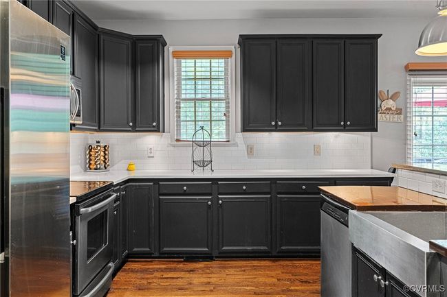 Kitchen featuring dark wood-style floors, dark cabinets, stainless steel appliances, and tasteful backsplash | Image 6
