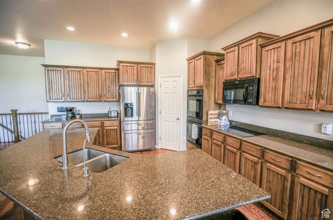 Kitchen featuring black appliances, a sink, a large island with sink, brown cabinetry, and dark wood-style flooring | Image 12