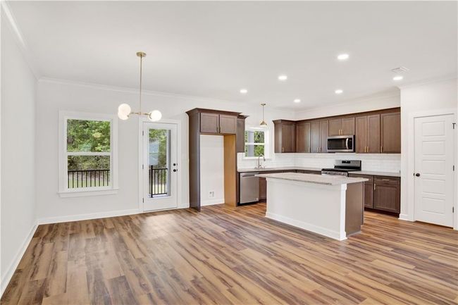 Kitchen with dark brown cabinetry, appliances with stainless steel finishes, decorative backsplash, wood finished floors, and a kitchen island | Image 10