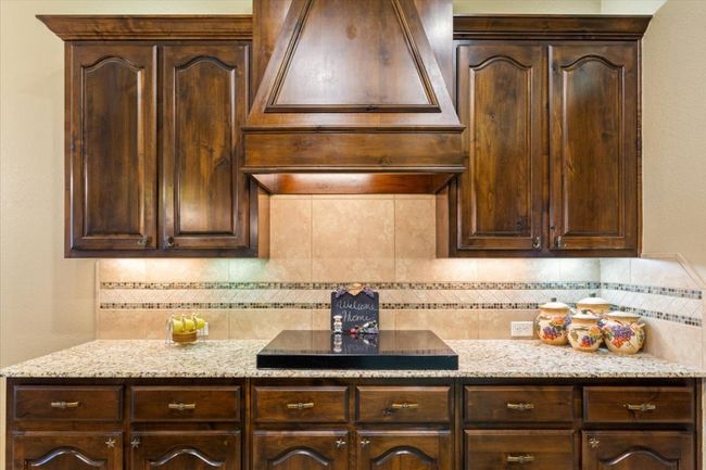 Kitchen with light stone countertops, backsplash, and dark brown cabinets | Image 17