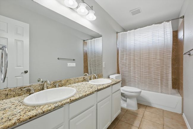 Bathroom featuring tile patterned flooring, toilet, double vanity, and shower / tub combo with curtain | Image 24