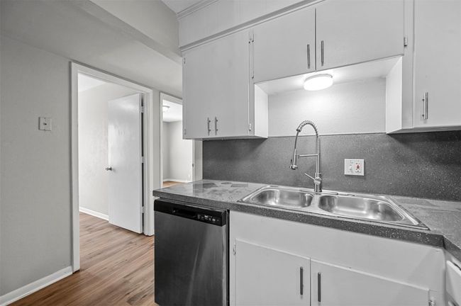 Kitchen with dishwasher, dark countertops, wood finished floors, and white cabinets | Image 4