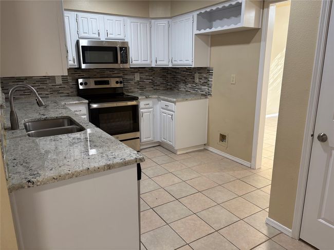 Kitchen with decorative backsplash, appliances with stainless steel finishes, a sink, light stone counters, and light tile patterned floors | Image 8