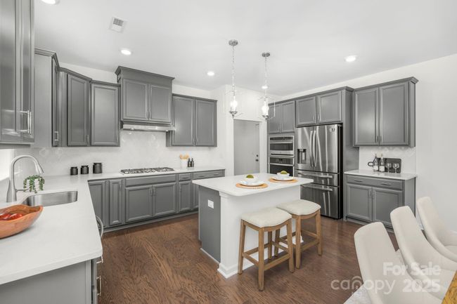 Upgraded kitchen with island, quartz countertops and tile backsplash. Oversized 36" cooktop, double ovens including a smart convection oven/microwave combo and a wall oven | Image 11