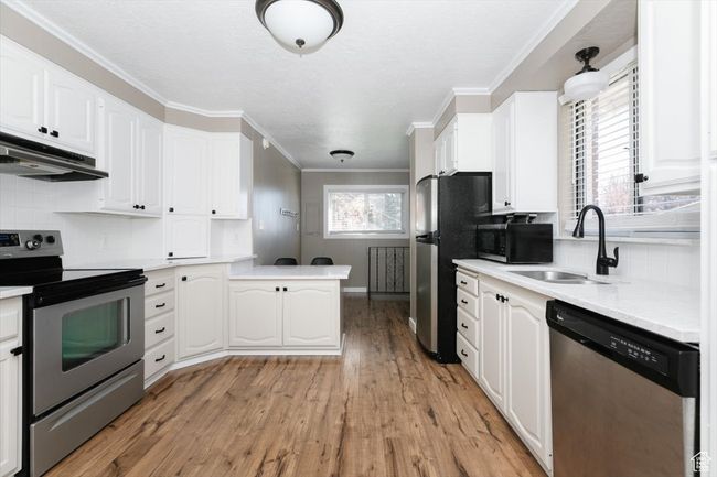 Kitchen featuring stainless steel appliances, under cabinet range hood, dark wood-style flooring, a peninsula, and crown molding | Image 11