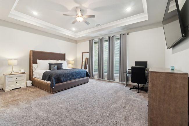 Carpeted bedroom featuring a tray ceiling, an office area, crown molding, ceiling fan, and recessed lighting | Image 17