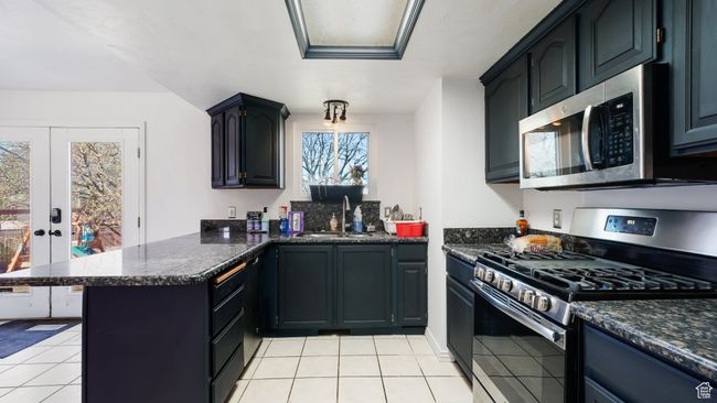 Kitchen featuring light tile patterned floors, stainless steel appliances, dark stone counters, a sink, and a peninsula | Image 10