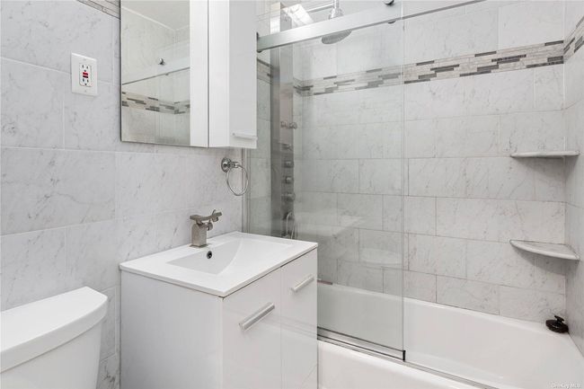 Full bathroom featuring bath / shower combo with glass door, vanity, toilet, and tile walls | Image 8
