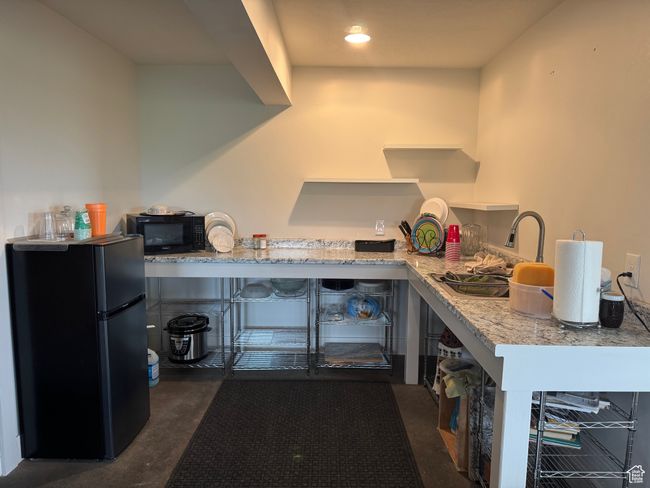 Basement kitchen with black appliances, concrete flooring, light stone counters, and a sink | Image 18