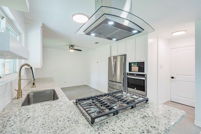 Kitchen featuring stainless steel appliances, island range hood, white cabinets, light stone counters, and light tile patterned flooring | Image 11