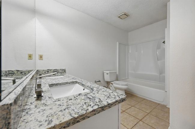 Bathroom with vanity, shower / washtub combination, tile patterned flooring, a textured ceiling, and toilet | Image 16