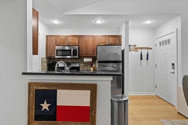 Kitchen with stainless steel appliances, dark countertops, light wood-type flooring, tasteful backsplash, and brown cabinets | Image 25