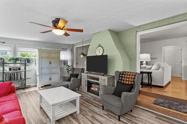 living room featuring brick wall, a ceiling fan, a glass covered fireplace, and wood finished floors | Image 11