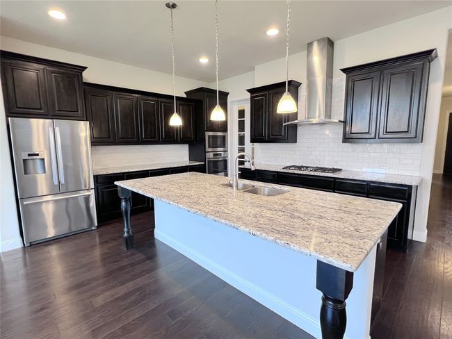 Kitchen with stainless steel appliances, wall chimney range hood, a kitchen bar, a center island with sink, and backsplash | Image 8