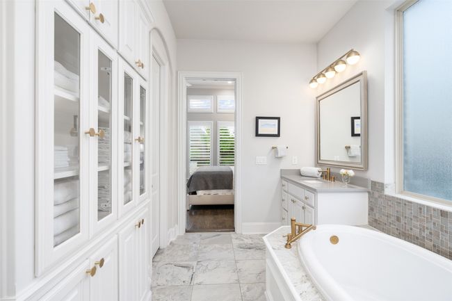 En suite primary bath with soaker tub, dual vanities, crushed quartz counters, upgraded tile backsplash, built in linen closet with glass display and upgraded light fixtures. | Image 20