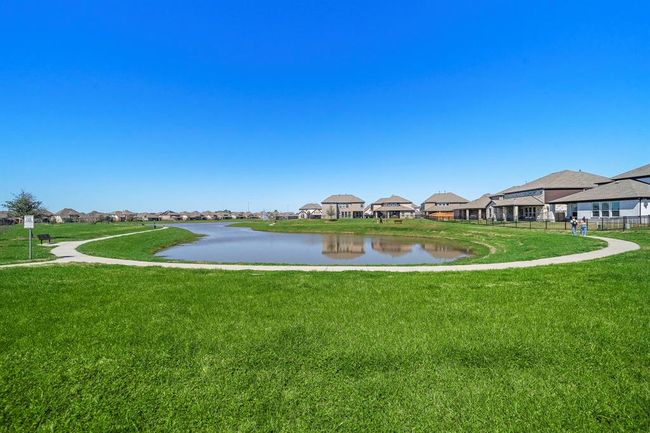 This photo showcases a serene neighborhood setting with a small pond surrounded by a walking path. The area is lined with modern houses and open green spaces, offering a peaceful suburban environment ideal for families and outdoor activities. | Image 23