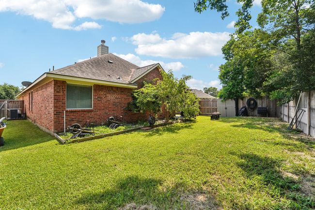 This photo showcases a spacious backyard featuring a brick house with a sloped roof. The yard is fenced, has lush green grass, and includes some trees, providing shade and privacy. Ideal for outdoor activities and relaxation. | Image 25