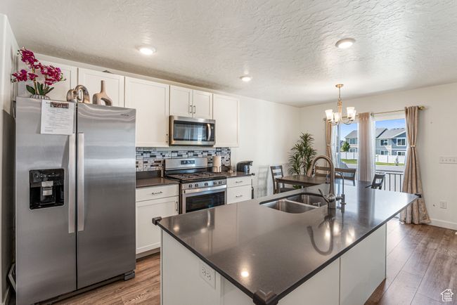 Kitchen featuring appliances with stainless steel finishes, a sink, dark countertops, a chandelier, and white cabinets | Image 11
