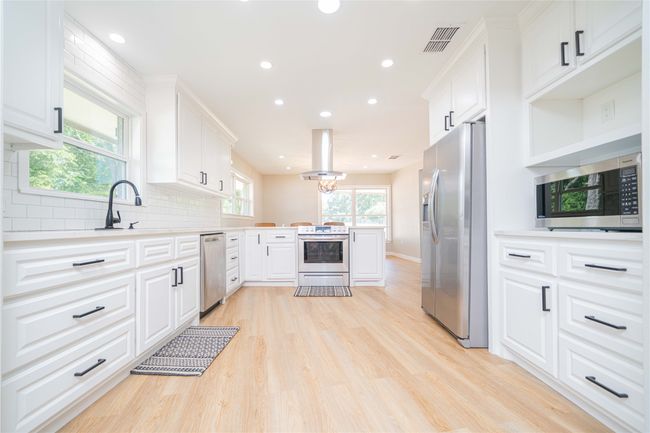 Kitchen featuring stainless steel appliances, island range hood, a peninsula, light wood-style flooring, and light countertops | Image 12