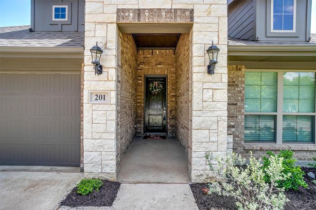 View of exterior entry featuring stone siding, a shingled roof, and an attached garage | Image 4