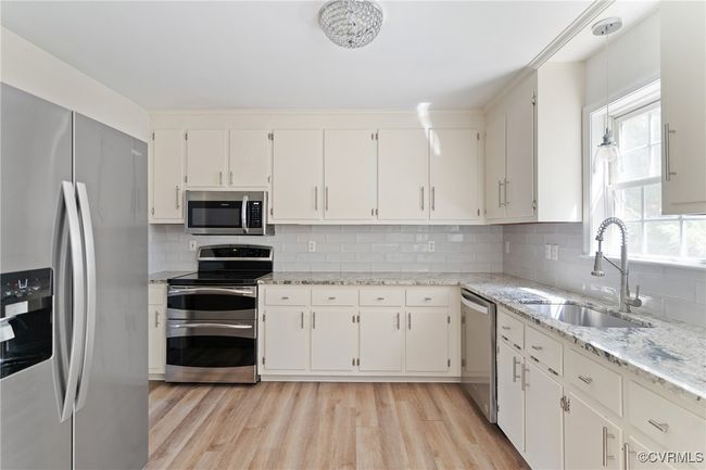Kitchen featuring appliances with stainless steel finishes, light wood-style flooring, decorative backsplash, and white cabinetry | Image 9