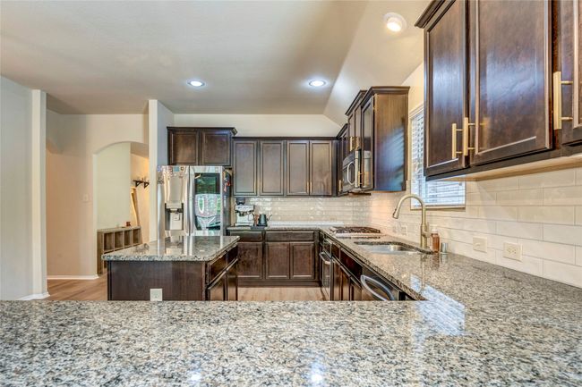 Kitchen with dark brown cabinetry, light stone countertops, light wood-style floors, appliances with stainless steel finishes, and arched walkways | Image 14