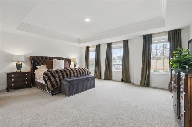 Expansive primary bedroom retreat featuring double entry doors, a tray ceiling, plush carpeting, and oversized windows that fill the room with natural light. The spacious layout offers plenty of room for a seating area or additional furniture. | Image 20