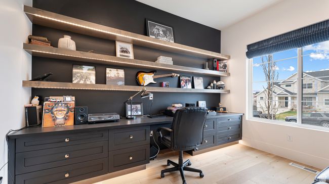 Home office with built in study area, baseboards, light wood finished floors, and visible vents | Image 11