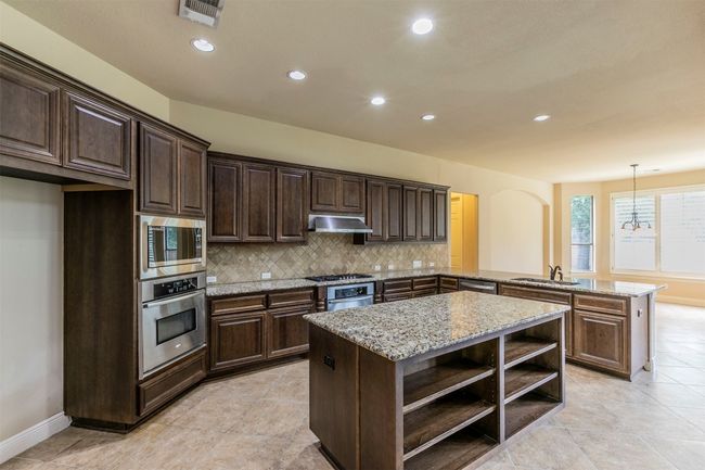 Kitchen featuring under cabinet range hood, stainless steel appliances, open shelves, a sink, and an island | Image 39