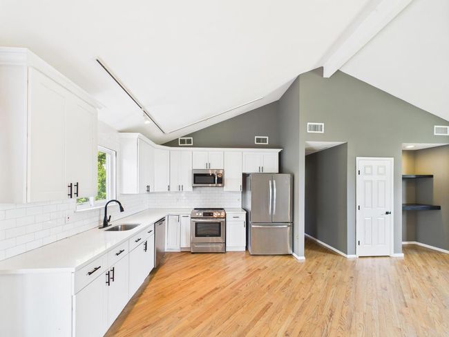 Kitchen featuring appliances with stainless steel finishes, light wood-type flooring, white cabinetry, light countertops, and tasteful backsplash | Image 6