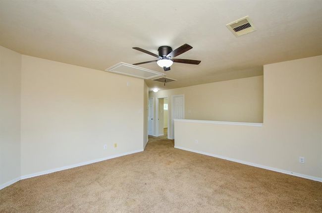 Game room features neutral walls and carpet, a ceiling fan, and a half-wall with a view into an adjoining space, offering an open and versatile layout. | Image 23