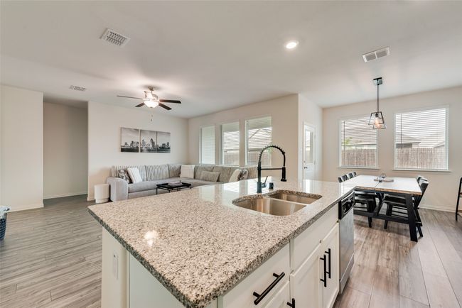 Kitchen featuring a center island with sink, hanging light fixtures, light wood-type flooring, ceiling fan, and white cabinetry | Image 5