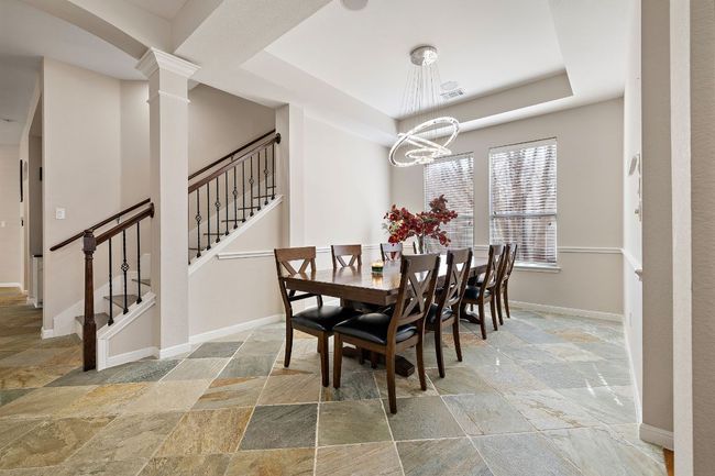 Dining space with decorative columns, stone tile flooring, a raised ceiling, stairway, and baseboards | Image 7